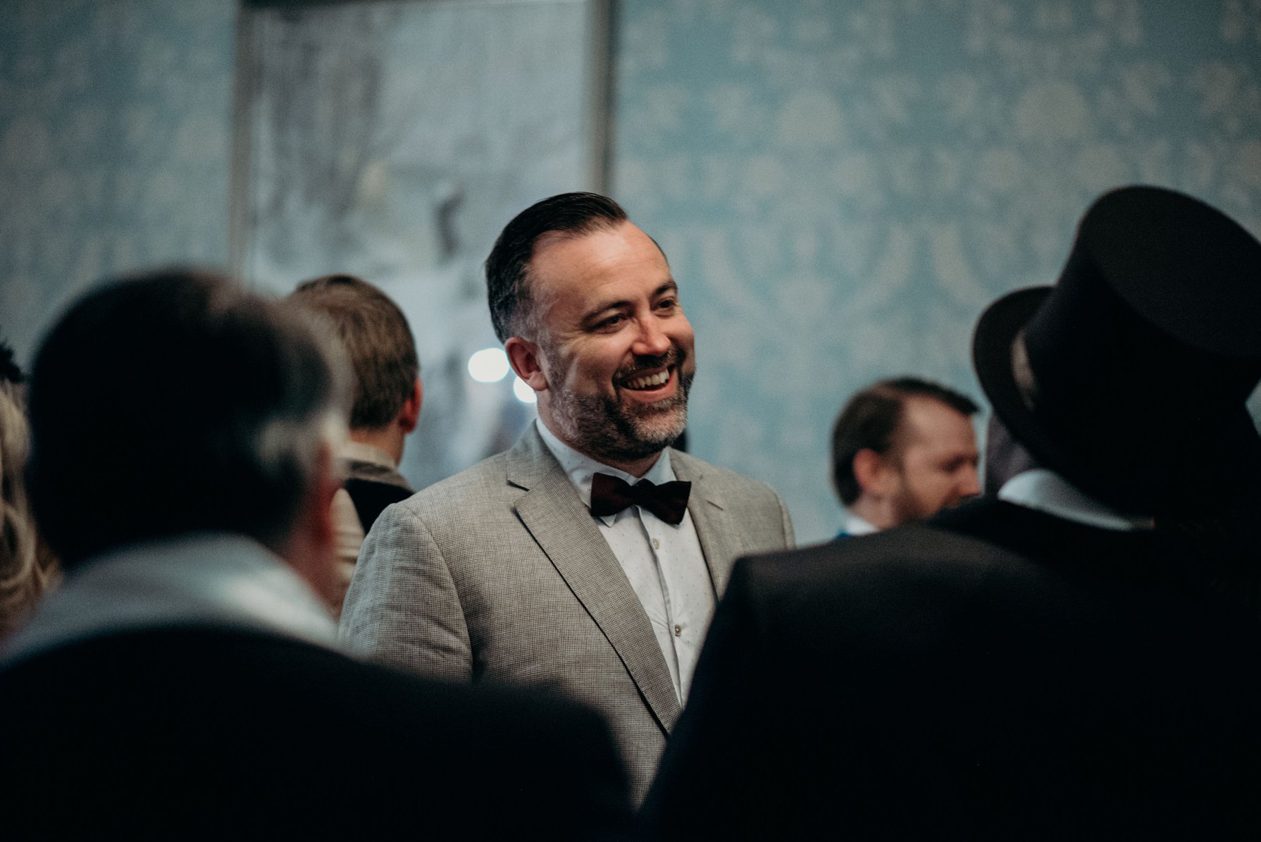 Smiling man in a light gray suit and black bow tie talking to a group of people at a formal event.
