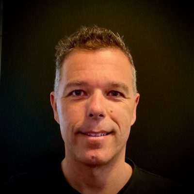 Portrait of a smiling man with short curly hair against a black background.