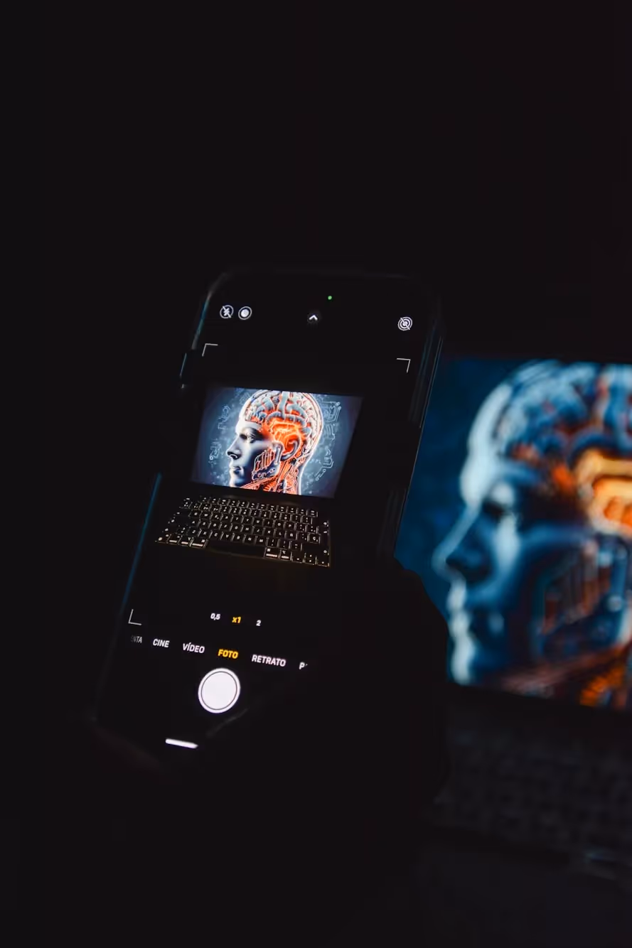 Dark photo showing a smartphone screen displaying a digital brain scan, with a glowing 3D brain illustration projected beside it, symbolizing AI and mobile technology.