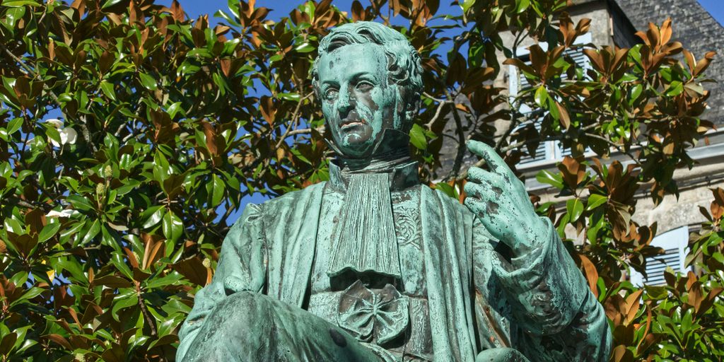 statue of man holding book under blue sky during daytime