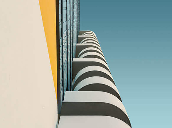 Low-angle view of modern building balconies with curved railings and yellow accent wall under blue sky.