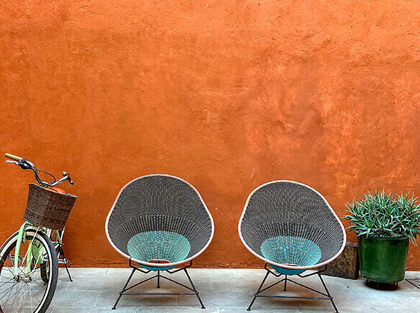 Two black and turquoise chairs, a green bicycle, and a green potted plant against an orange wall.