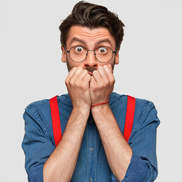 Man with glasses biting fists and wide eyes showing a nervous or anxious expression.