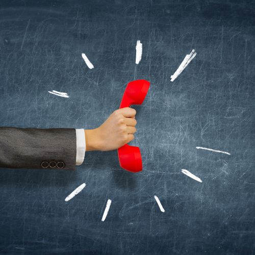 Hand in a suit holding a red telephone handset against a chalkboard background with white chalk lines radiating outward.