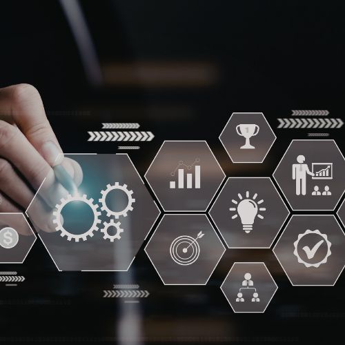 Hand interacting with virtual hexagonal icons representing business concepts like gears, bar chart, trophy, target, light bulb, presentation, hierarchy, and quality check.