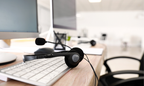 Black headset with microphone resting on a white keyboard on a wooden desk in a modern office.