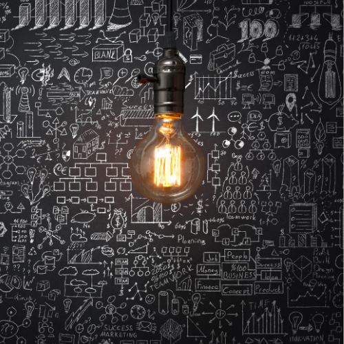 Glowing vintage light bulb hanging in front of a blackboard filled with white business and marketing sketches.