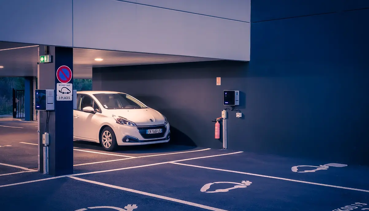 Borne de recharge Qovoltis sur le parking d'une entreprise, véhicule électrique en charge