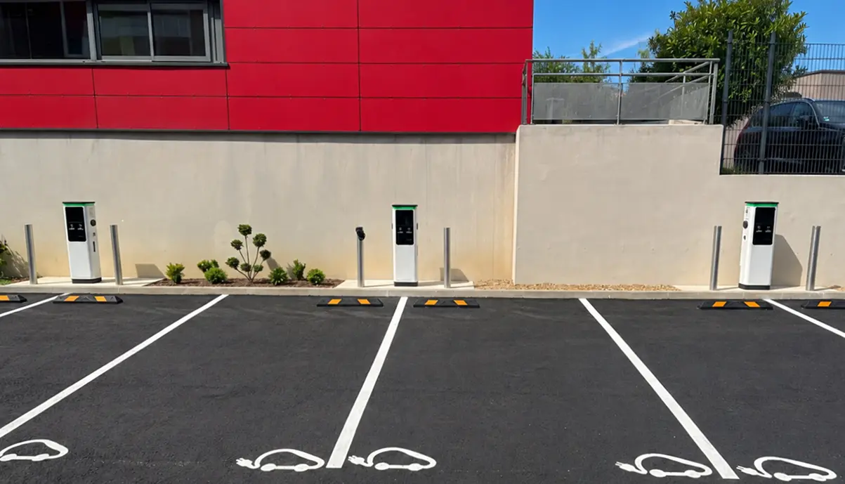 Trois bornes de recharge Qovoltis installées sur un parking avec places réservées aux véhicules électriques