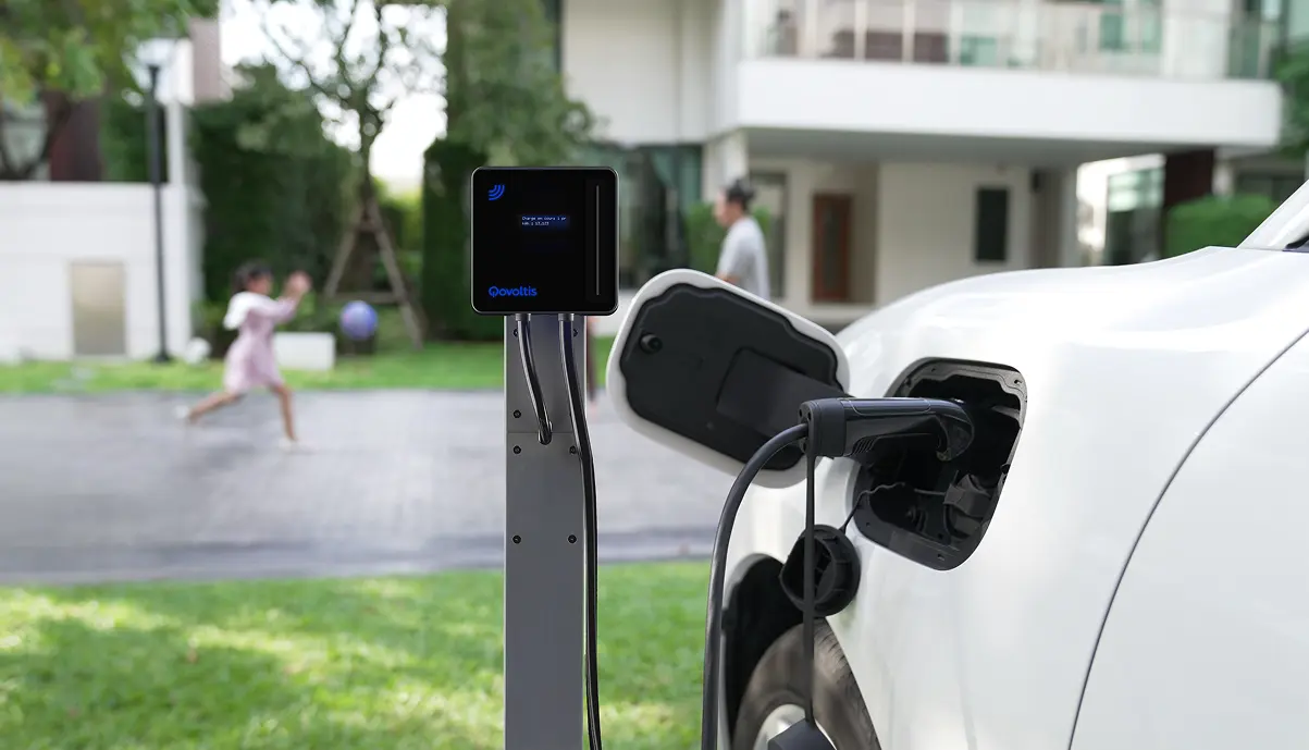 Borne de recharge Qobox mini installée devant une maison, branchée sur une voiture électrique blanche