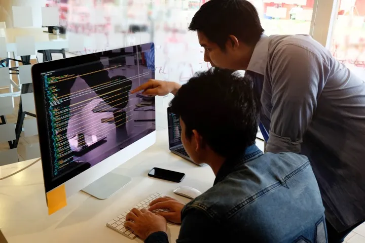 Dos hombres mirando un computador con un código.