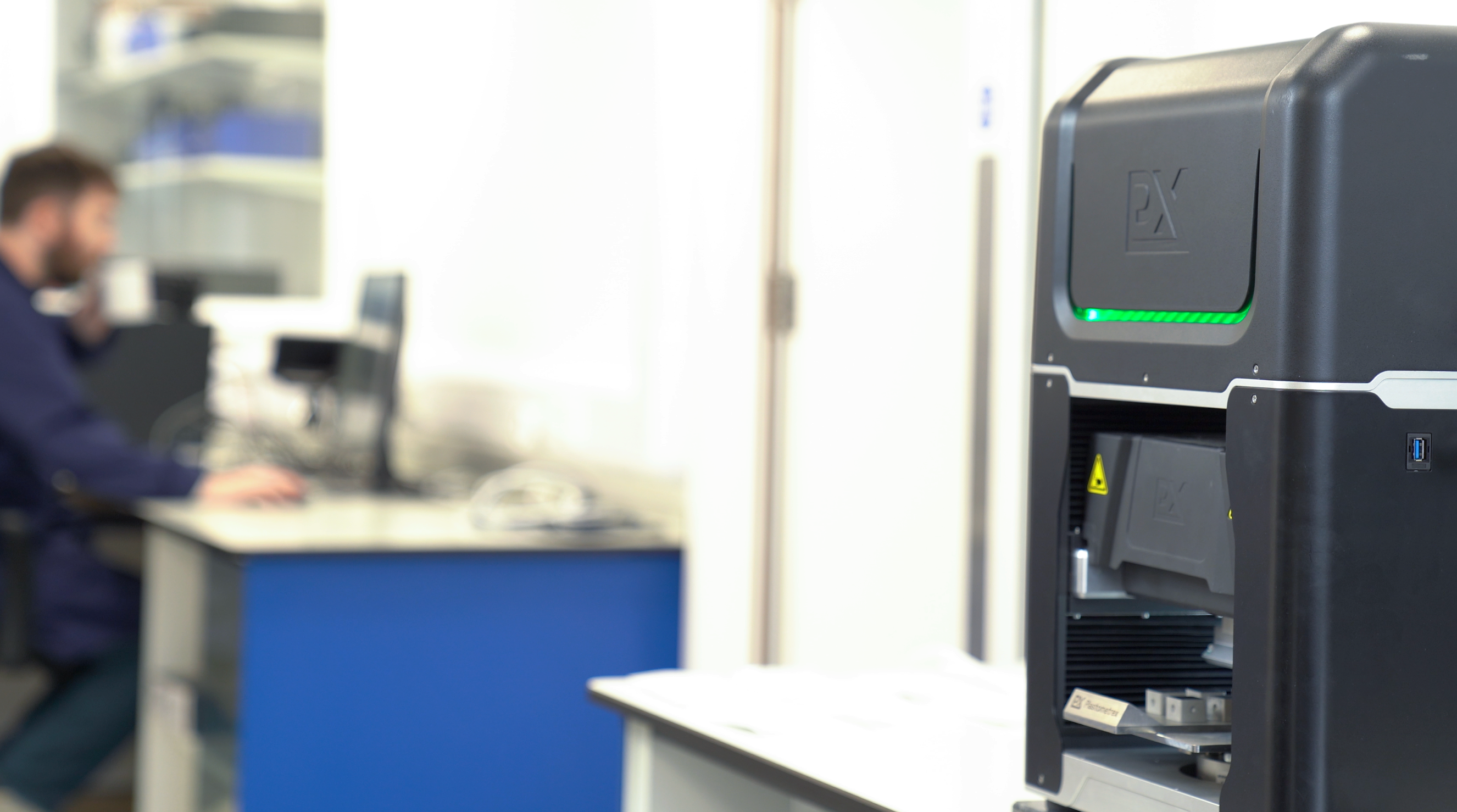 PLX-AutoStage running an unattended PIP testing sequence in a lab while an engineer works at a desk in the background.