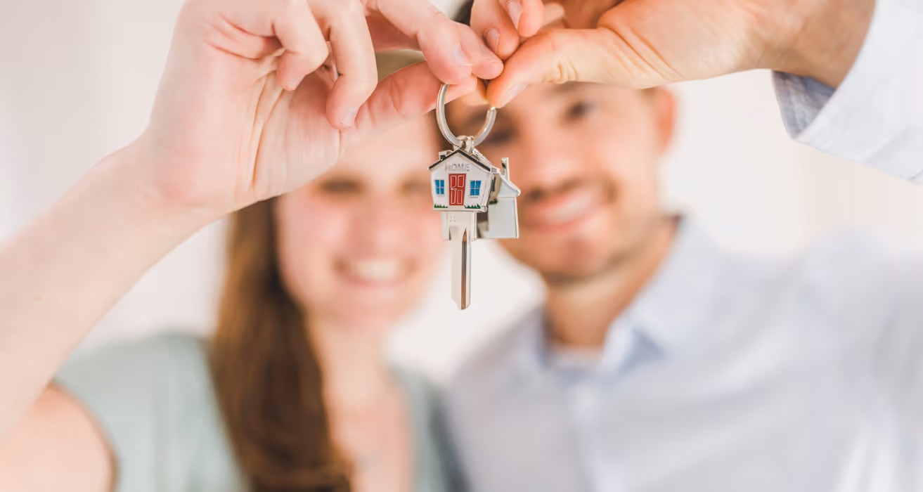 Happy couple holding a house-shaped keychain with a key, symbolizing new homeownership and a successful home purchase.