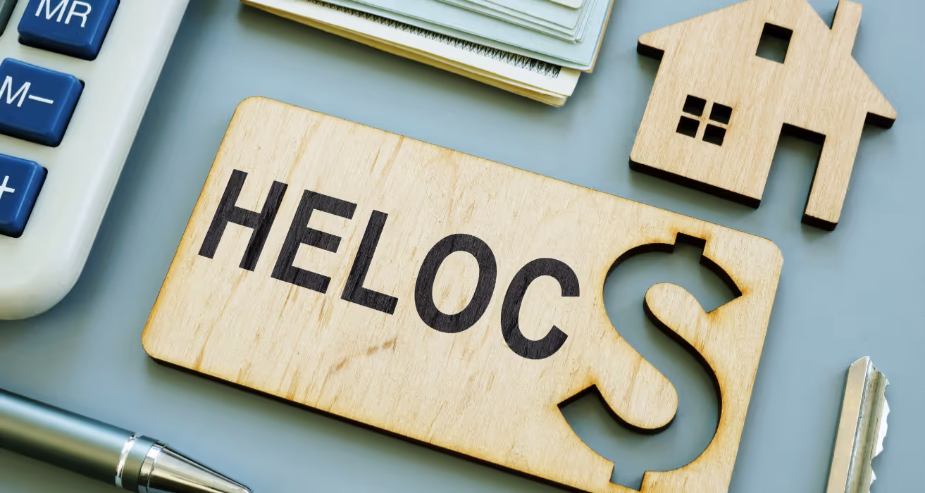 Wooden HELOC sign with dollar symbol, house cutout, money, pen, and calculator representing home equity line of credit concept.