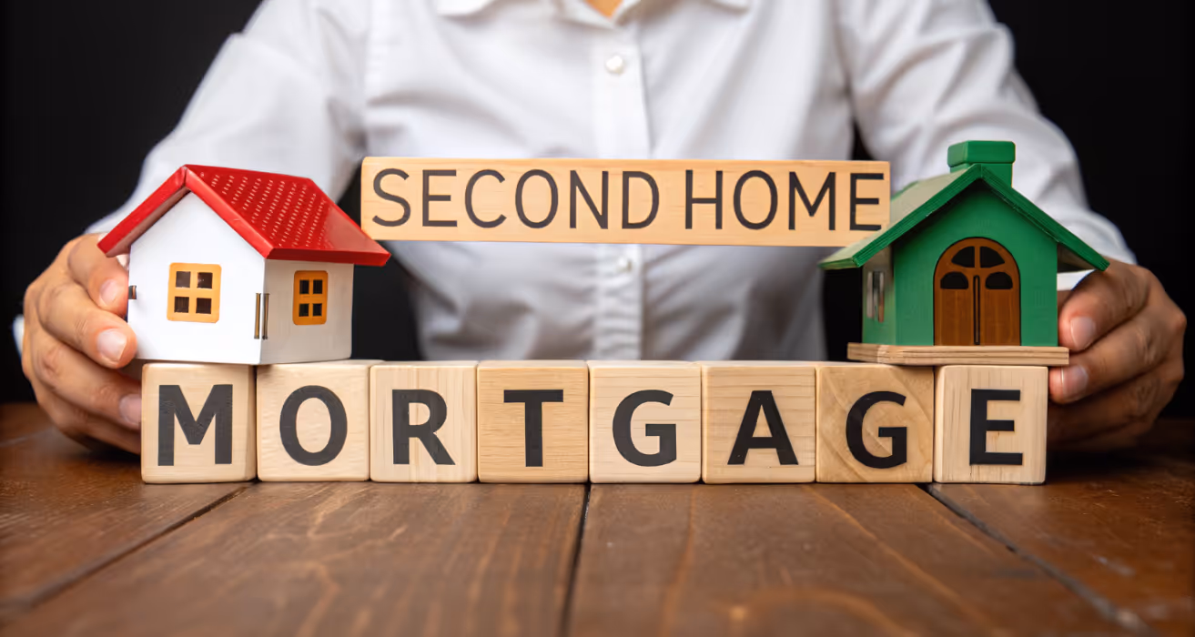 Person holding model houses with "SECOND HOME INVEST" text, representing decisions around refinancing a second home mortgage.