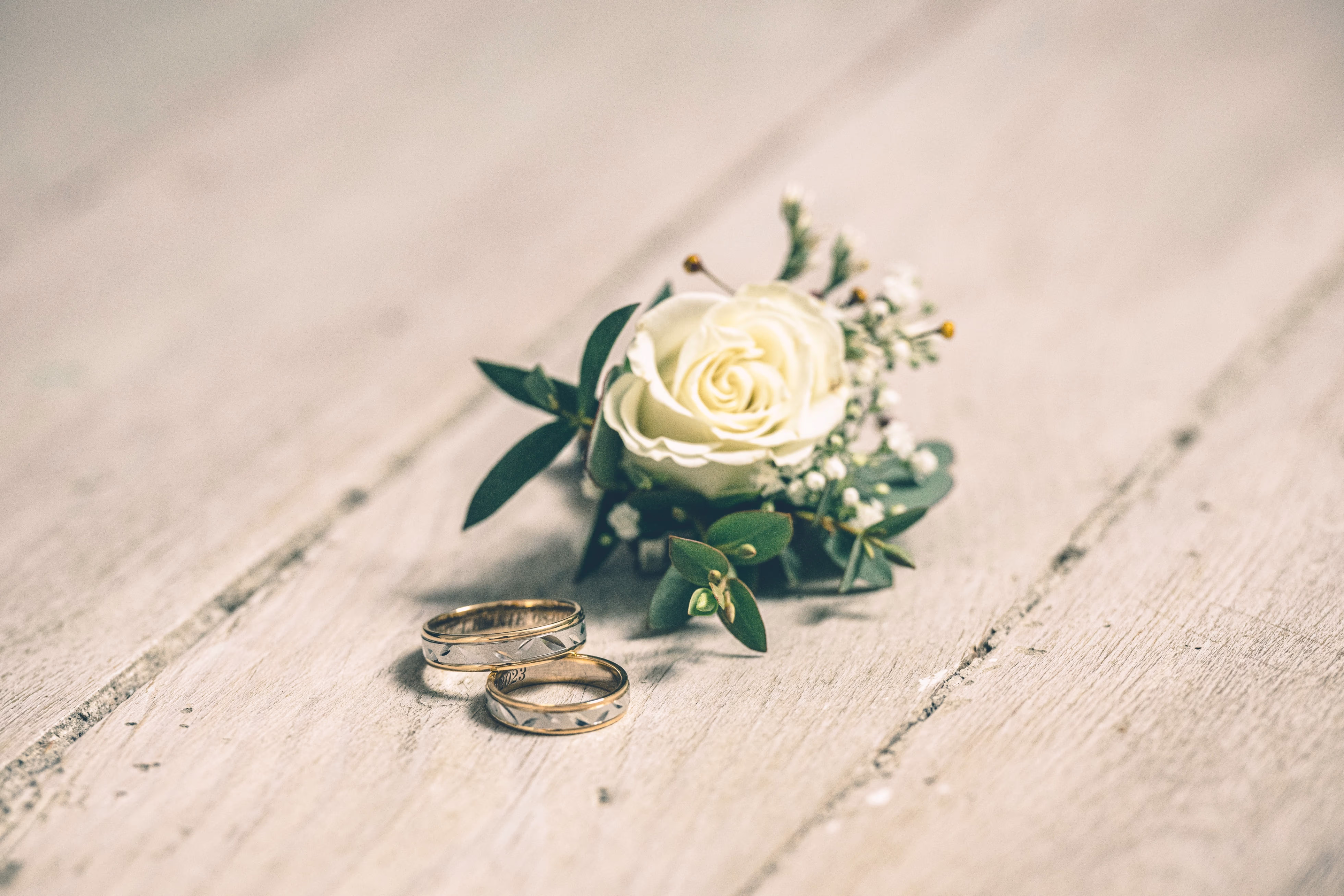 Une rose jaune pâle et deux alliances posées sur un beau parquet