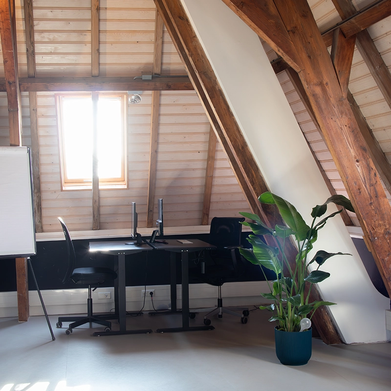 Een whiteboard, 2 bureaus met stoelen en een computer en een kamerplant