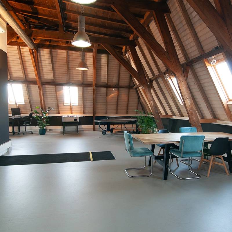 Een kantoor zolder met verschillende werkplekken en een eettafel.