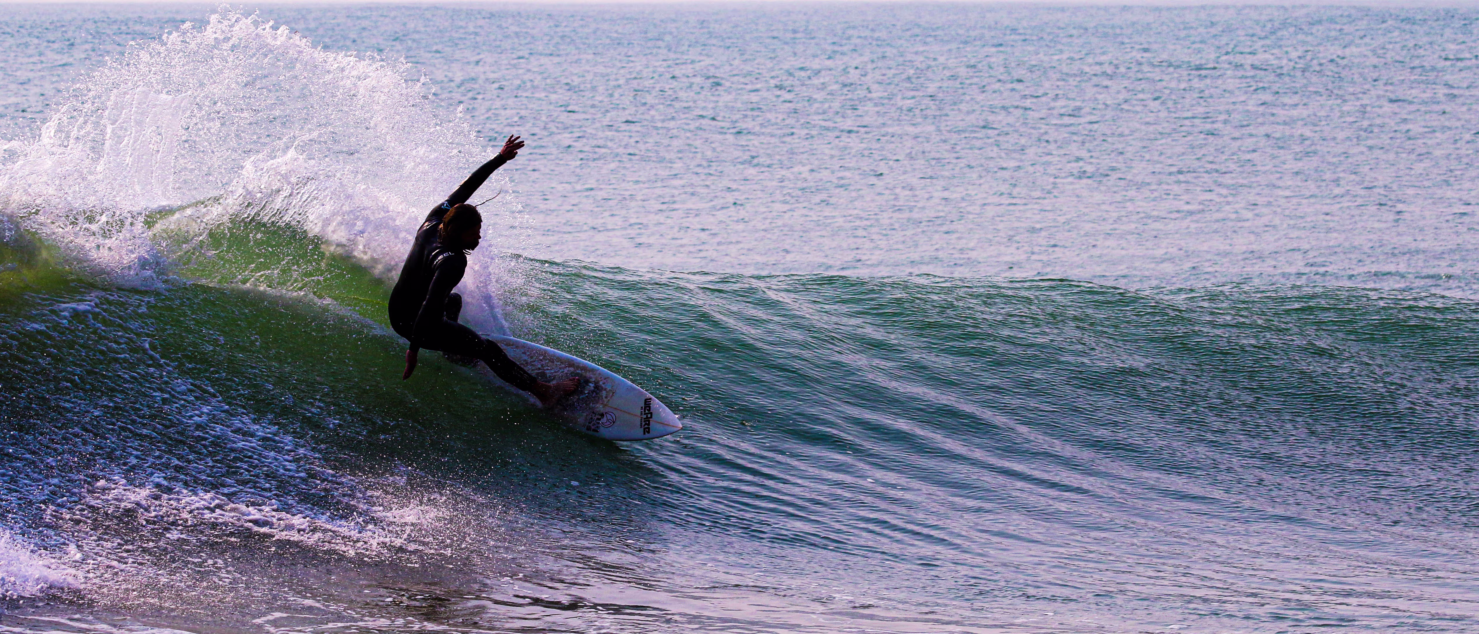 Surferin reitet kraftvoll eine türkisfarbene Welle entlang der steilen Klippen von Cabo Ledo, Angola