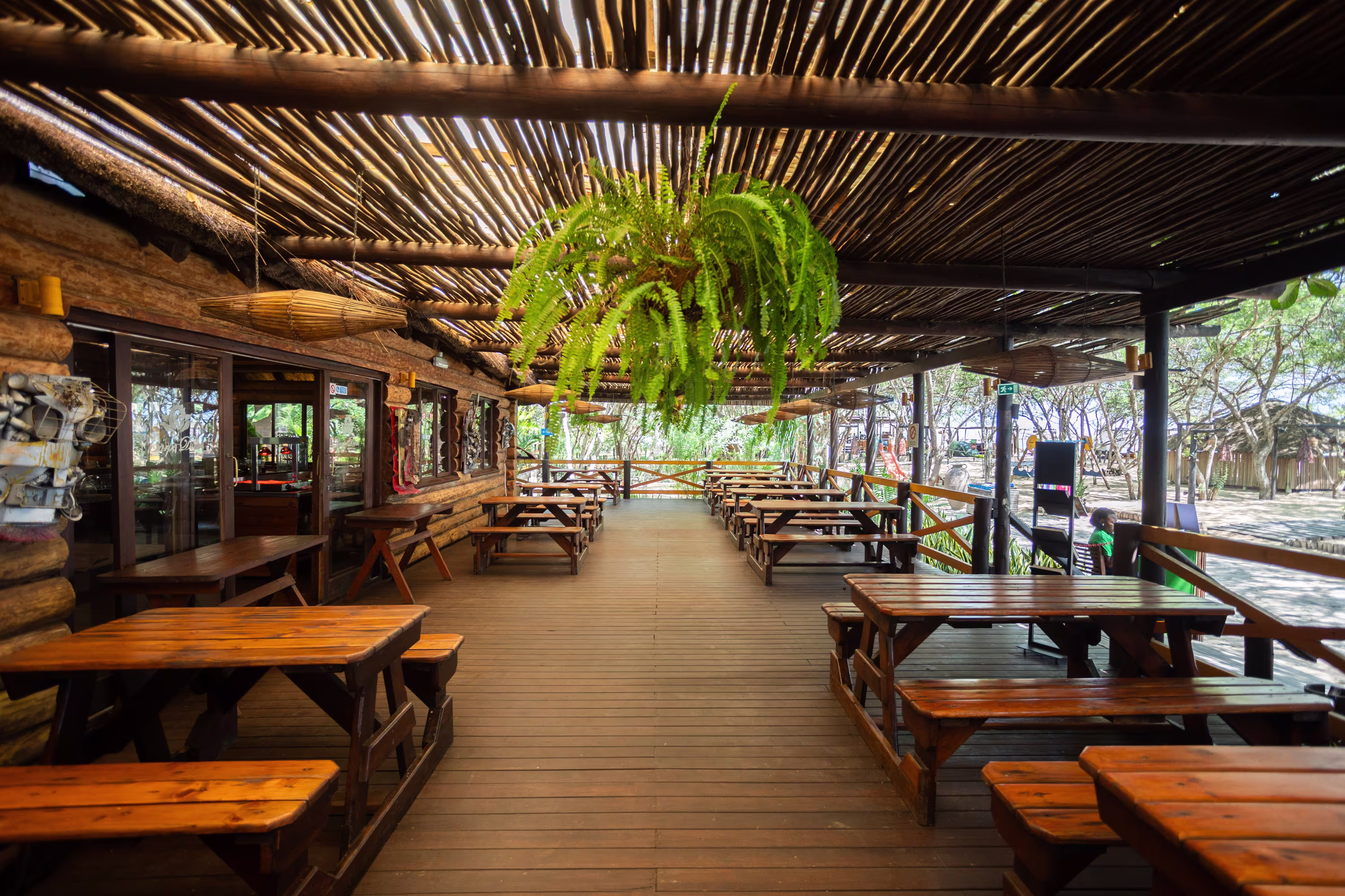 roßer, offener Speiseraum mit rustikalen Holztischen und -bänken unter einem gesprenkelten Bambusdach, umgeben von Farnen und Küstenbäumen am Carpe Diem Resort in Cabo Ledo.