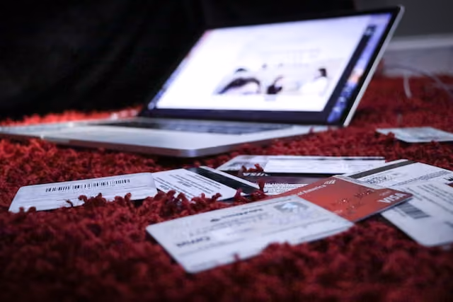 Open laptop on red carpet surrounded by airline tickets, passport, and pen, suggesting travel planning or booking.
