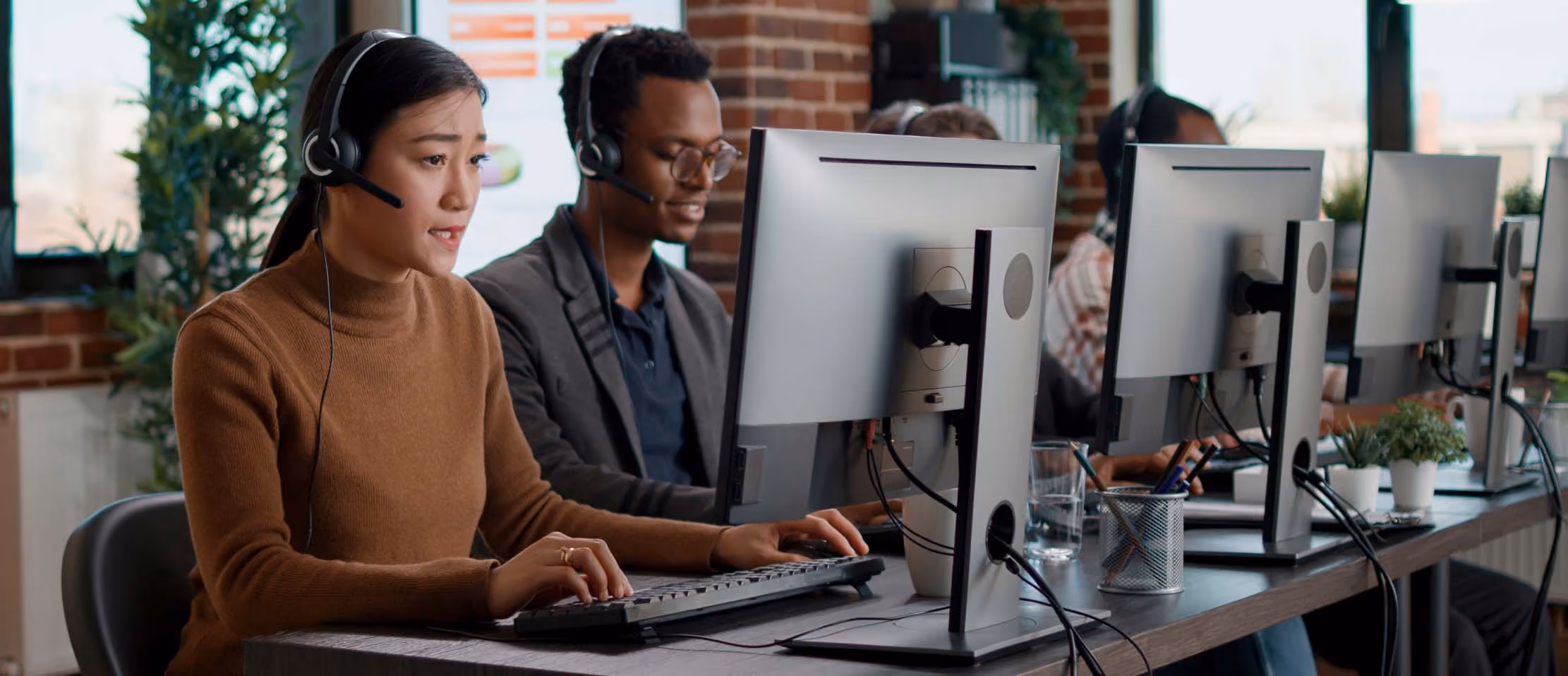 Customer support team working at computers with headsets in modern office, focused on assisting clients efficiently.