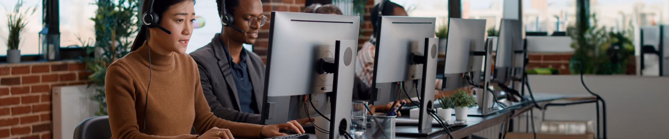 Customer support team working at computers with headsets in modern office, focused on assisting clients efficiently.