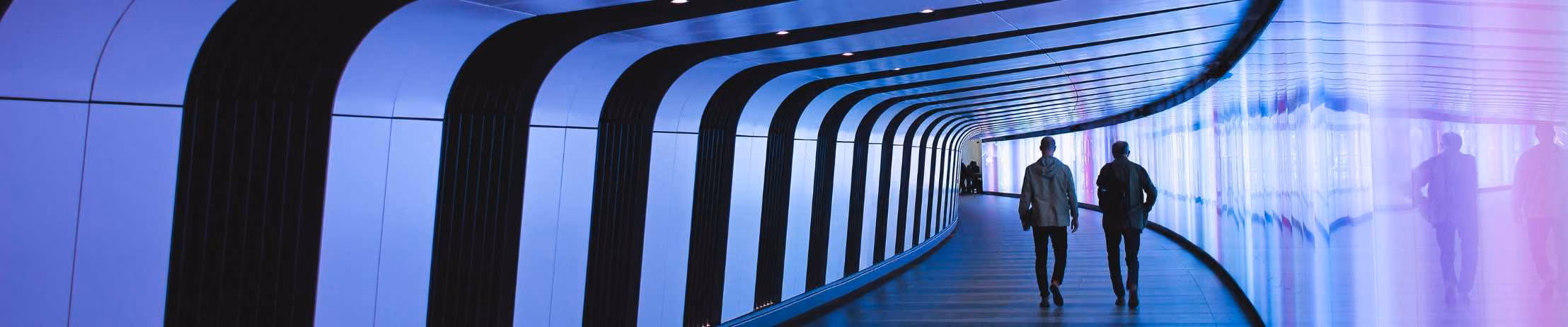 Futuristic tunnel with purple lights, two people walking, modern architecture.