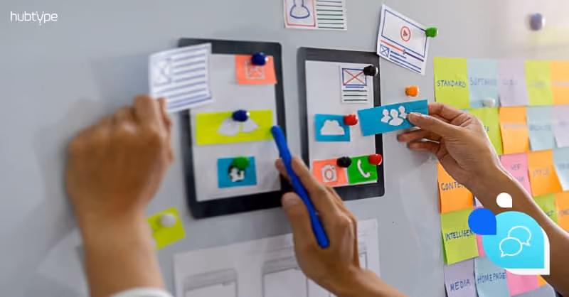 Hands arranging UI design wireframes and colorful sticky notes on a whiteboard, illustrating a creative app development process.