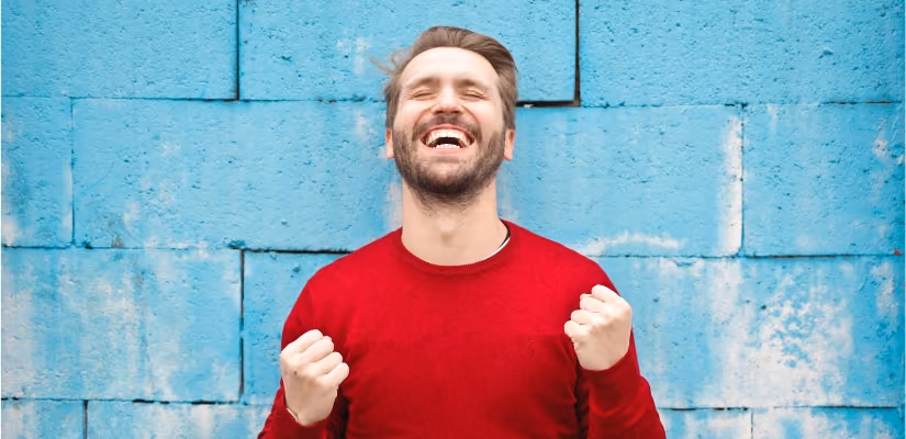 Man in red sweater smiling broadly against a blue wall, illustrating positive customer service experience.