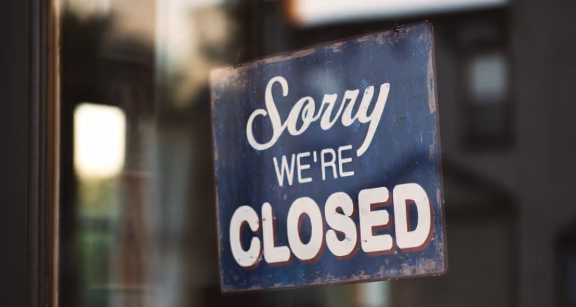Sorry we're closed sign on a glass door, symbolizing business closures.