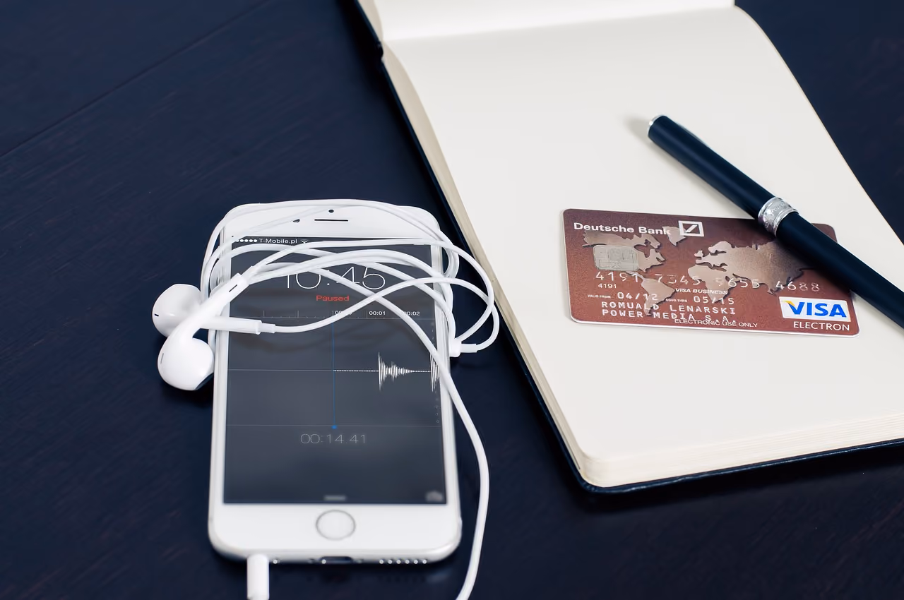 Smartphone with earphones next to credit card and notebook, highlighting mobile technology and finance.