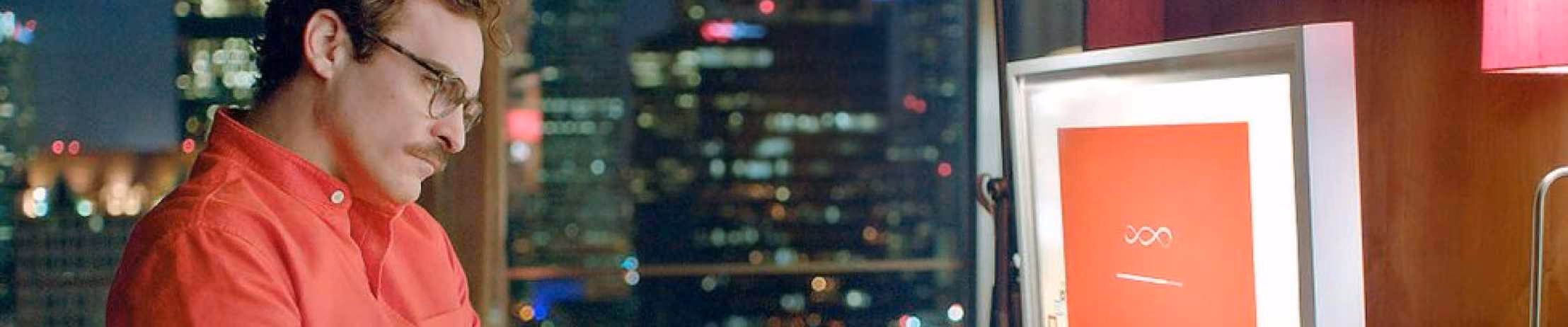 Man in red shirt at a desk with computer screen, overlooking cityscape at night. Perfect for tech and lifestyle articles.