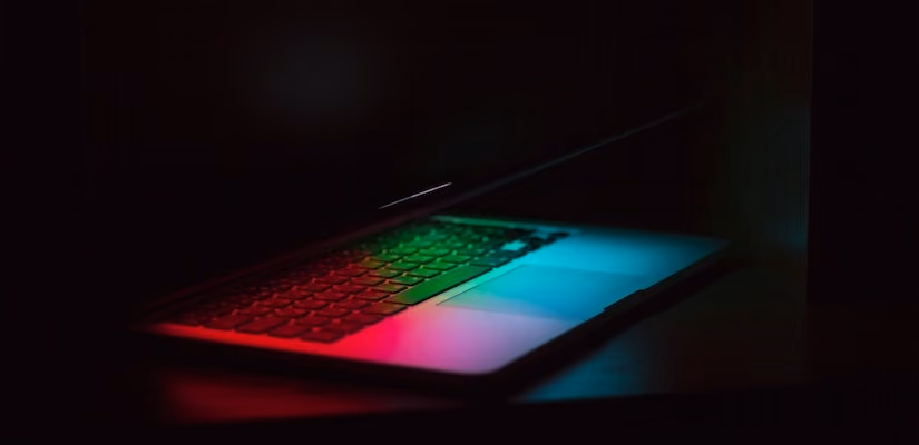 Laptop with colorful glow in dark room, ideal for digital transformation and chatbot technology articles.