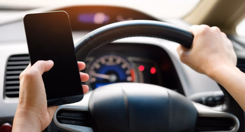 Driver holding phone while steering, highlighting distracted driving dangers.