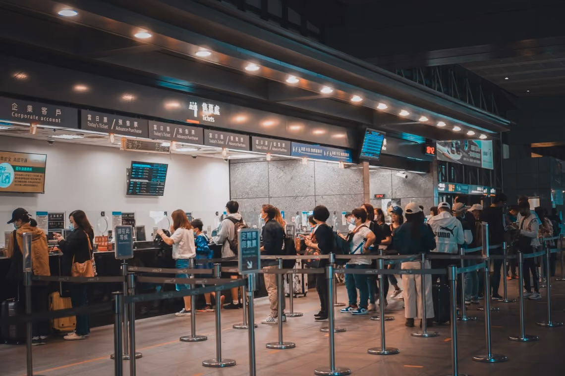 A group of people waiting in line at a ticket counter in a transportation hub, with signage in both Chinese and English indicating services like “Today’s Ticket” and “Advance Purchase.”