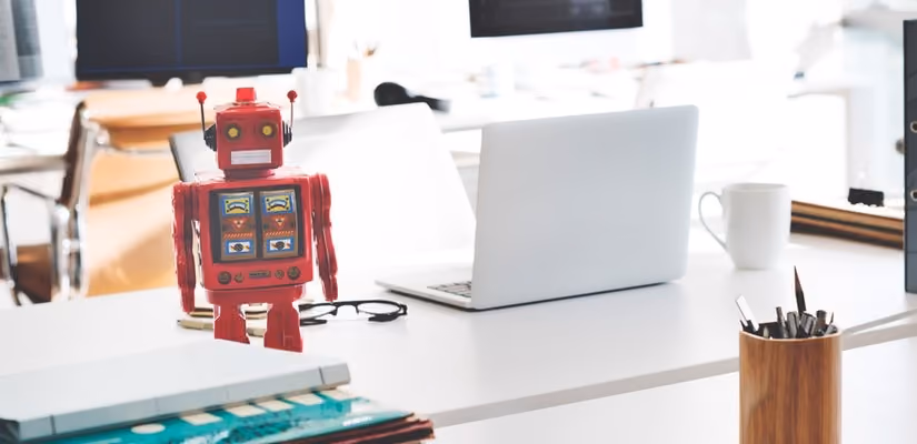 Chatbot robot toy on desk beside laptop, ideal for AI and customer service topics.