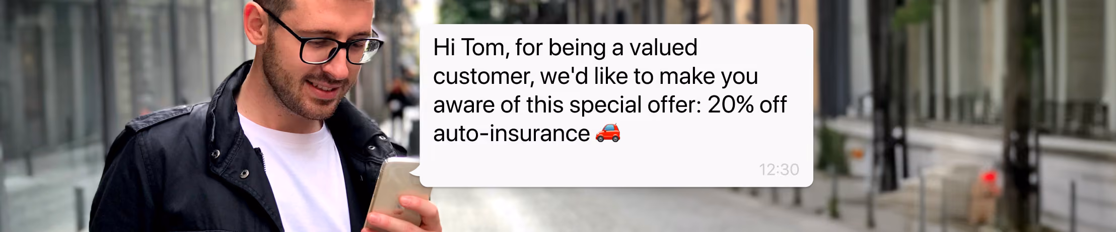 A smiling man wearing glasses and a black jacket stands on a city street while looking at his smartphone, which displays a message offering 20% off auto insurance, with options to “Request a simulation” or “Speak to an agent.”