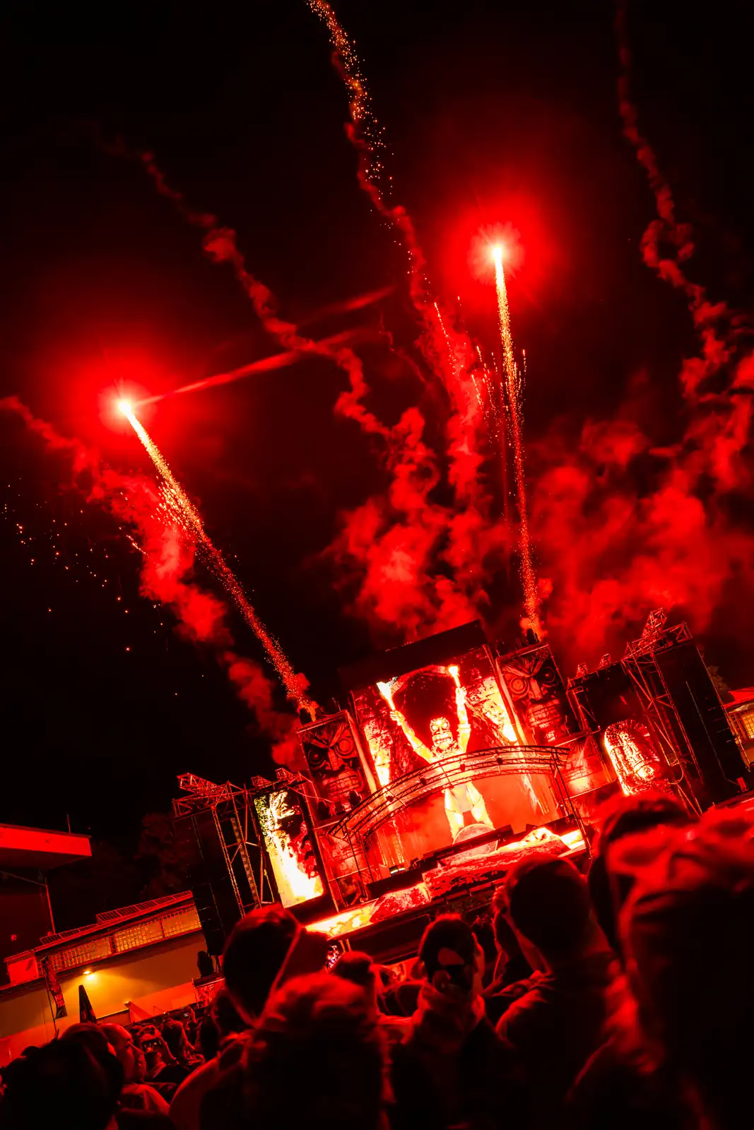 Menschenmenge vor einer Bühne mit intensiven roten Feuerwerkseffekten und einer großen Figur in der Mitte.