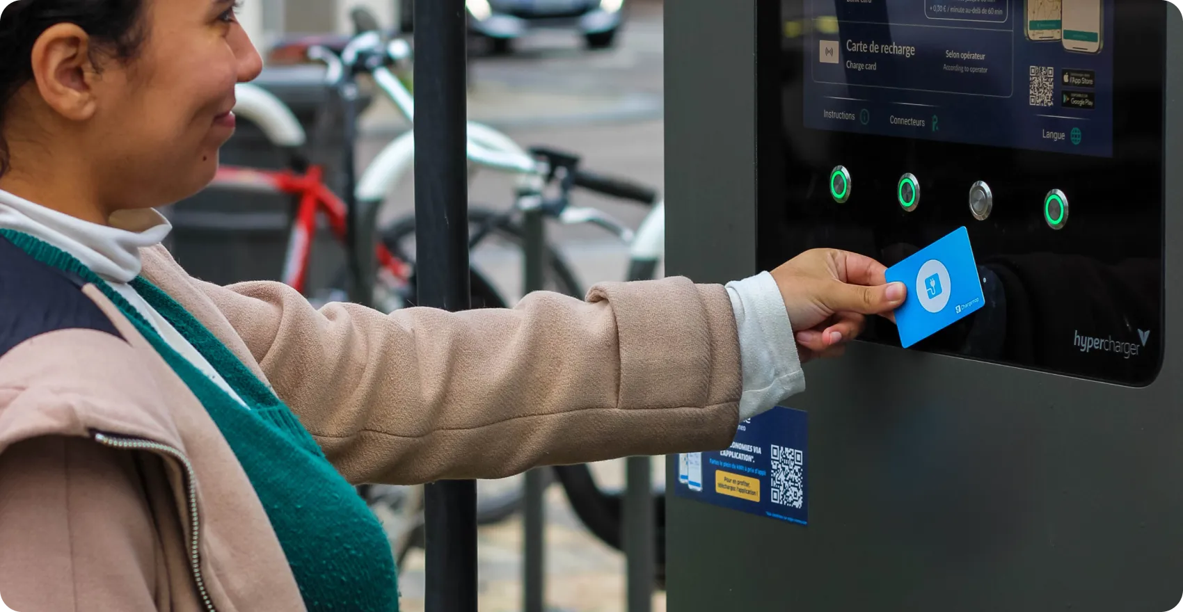 Personne détentrice d'une carte bleue à une borne de recharge de véhicule électrique Hypercharger pour paiement sans contact.