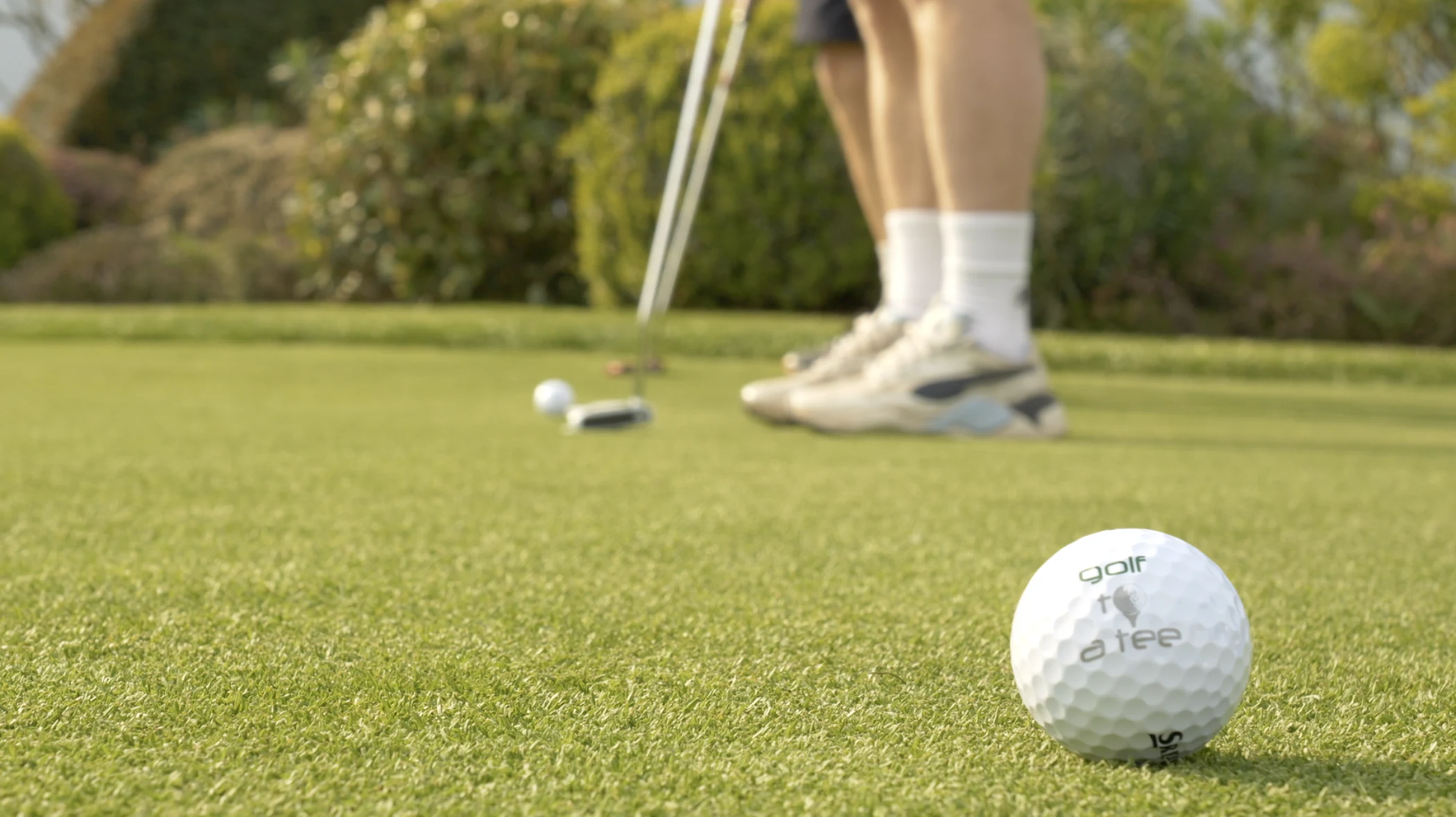 Golf ball on green with player's feet and club in background