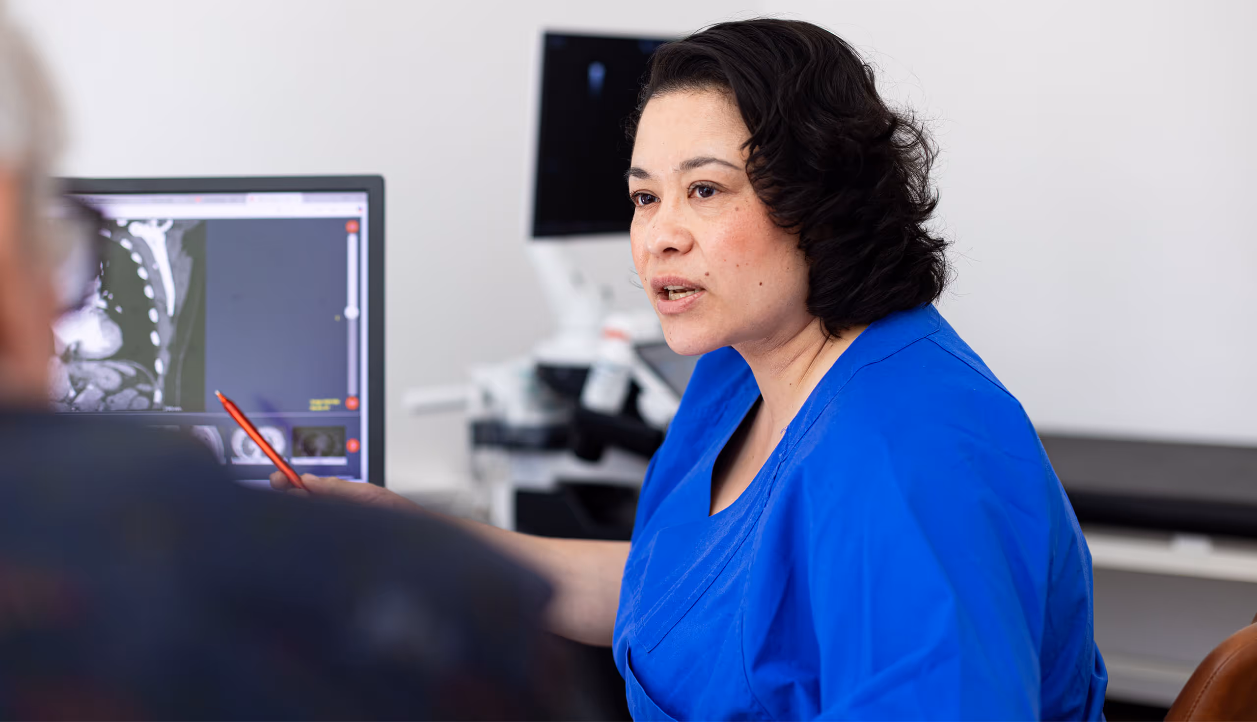 Ärztin im blauen Kittel erklärt einem Patienten medizinische Bilder auf einem Bildschirm.