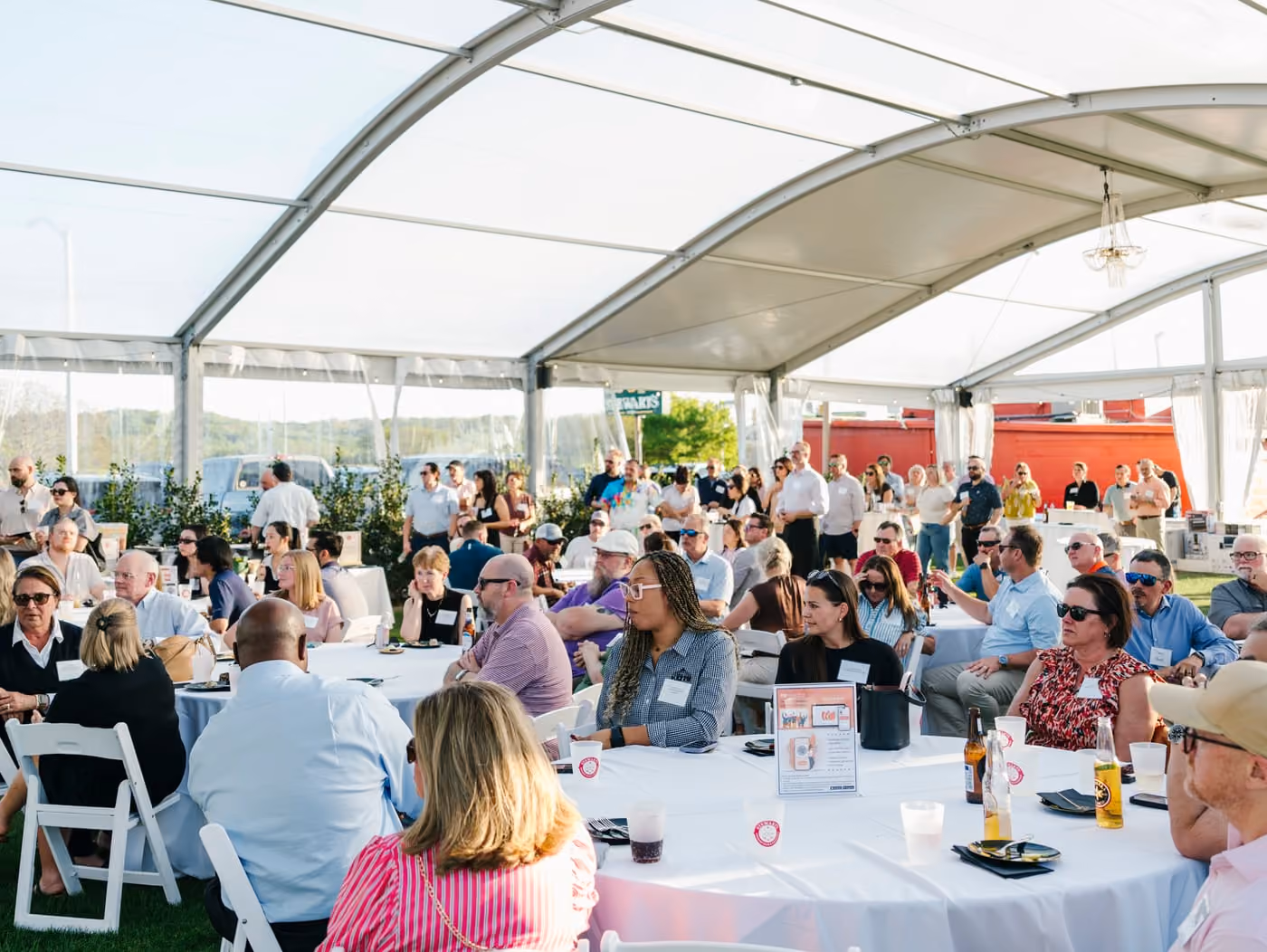 Guests seated at round tables under the clear-span tent at a corporate event