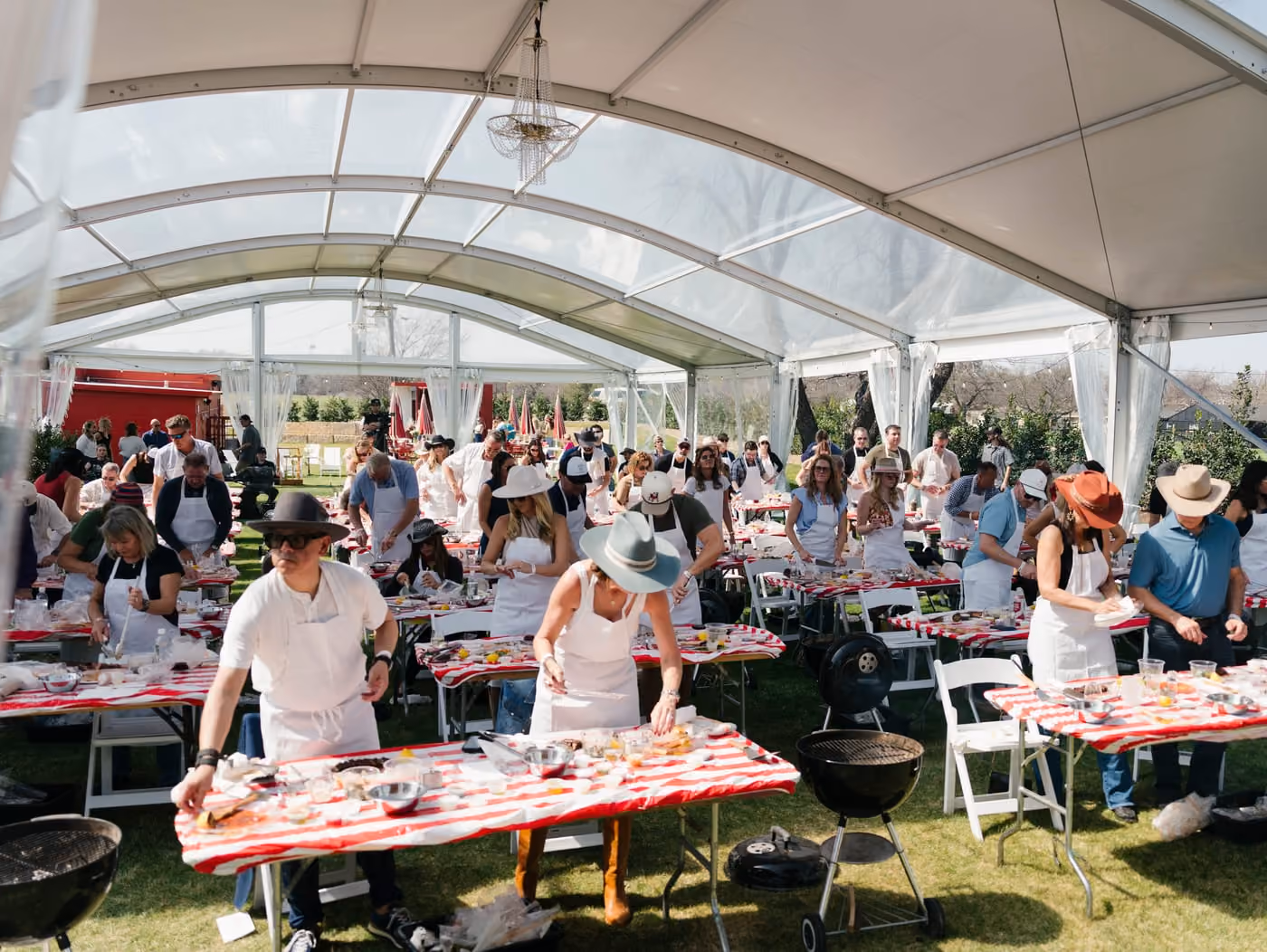 Chefs and guests at long tables during a hands-on cooking event under the tent