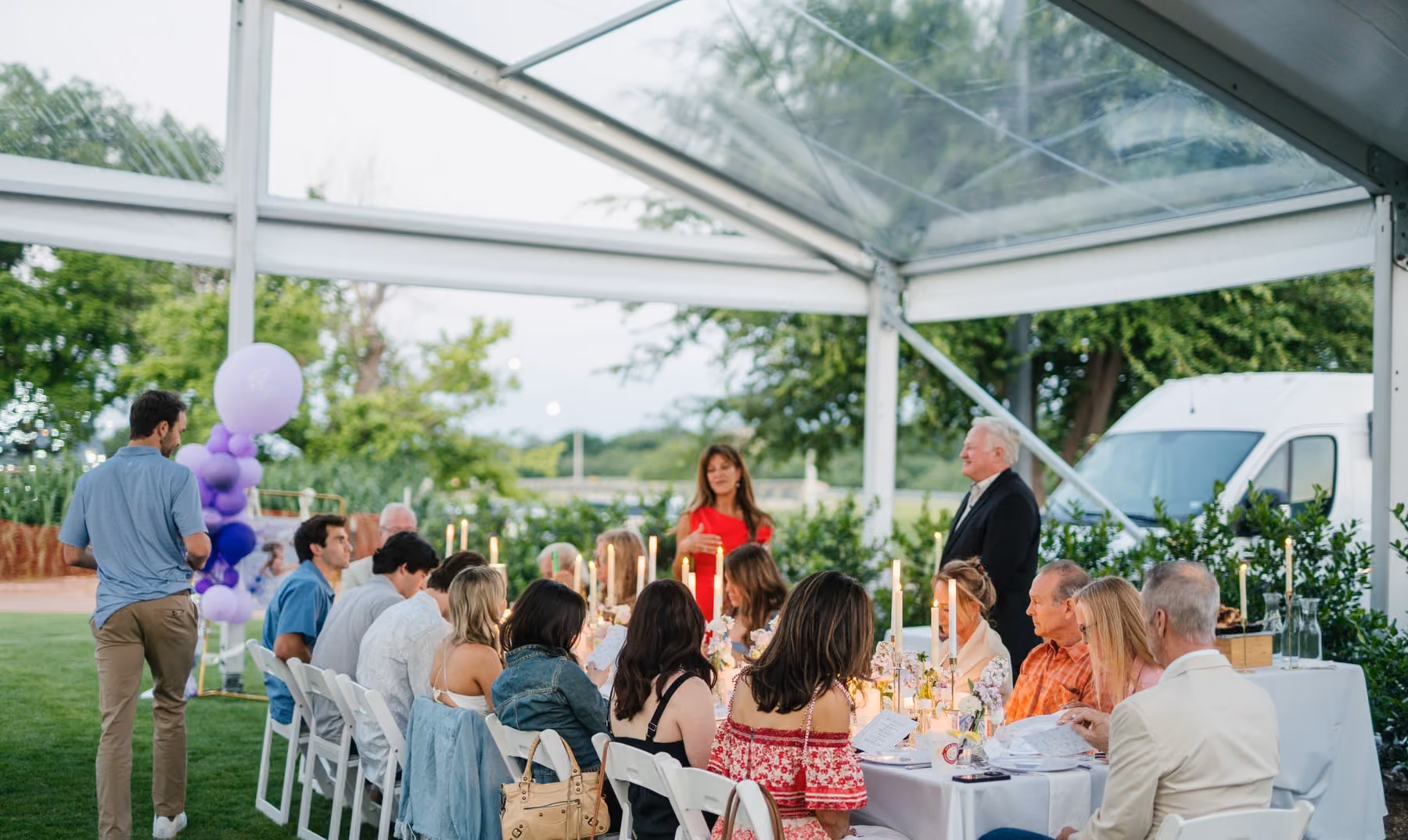 Guests seated at long tables under the covered lawn's clear-span tent