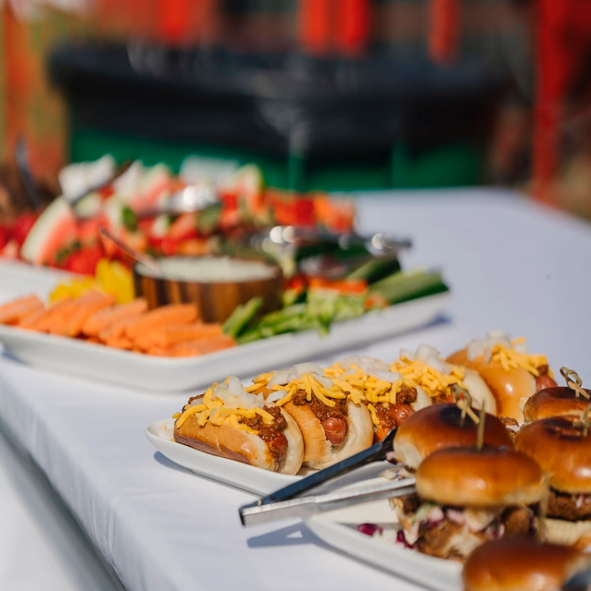 Catering spread of sliders, crudités and charcuterie on a long white table