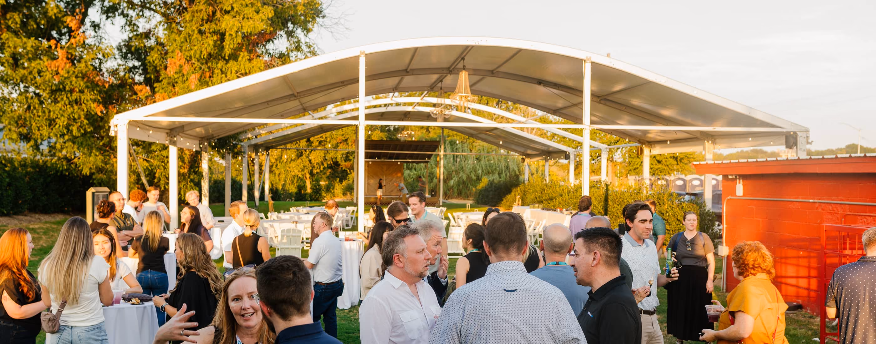 Guests with cocktails on the lawn at golden hour beside Stewart's event tent