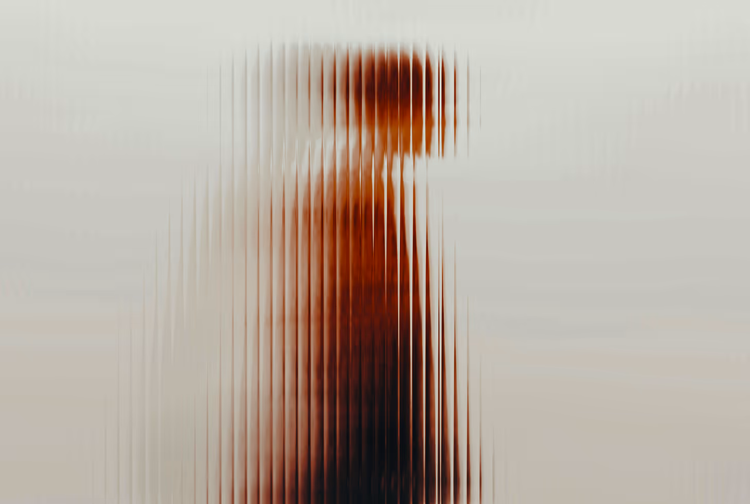 Silhouette of a person seen through vertically ribbed translucent glass creating a blurred striped effect.