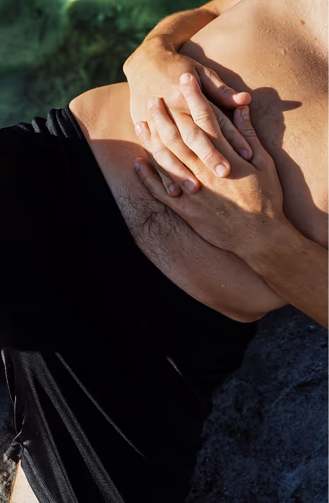 Close-up of a person wearing black shorts holding their aching side above the hip with both hands.