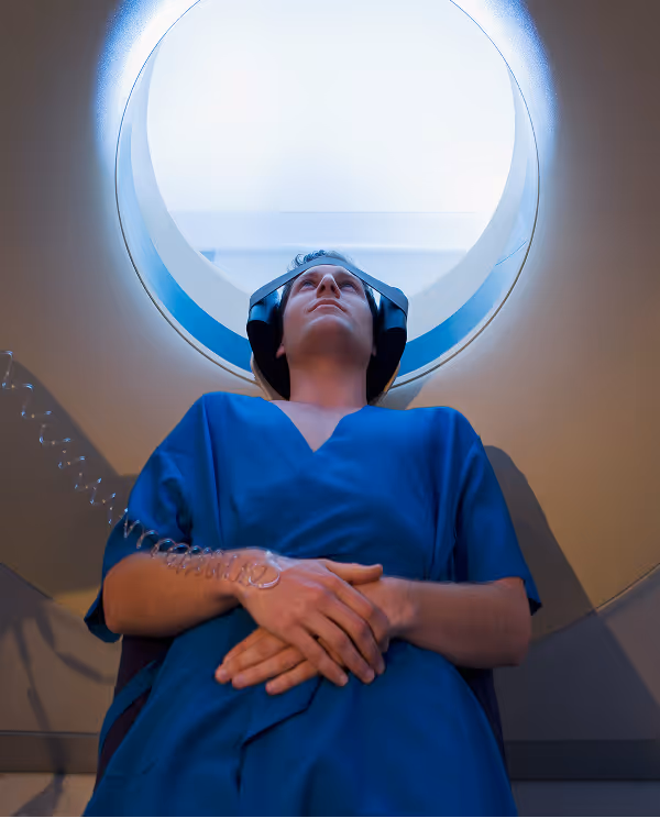 Patient in blue hospital gown lying inside a CT scan machine with a head restraint and connected to IV.